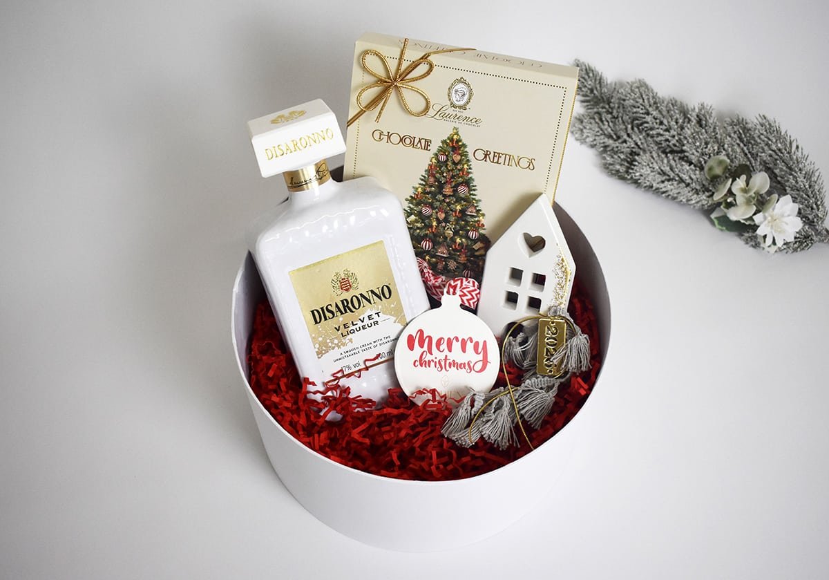 Festive Treasures — Στρογγυλή συσκευασία με ποτό, γλυκά και λευκό διακοσμητικό σπιτάκι.